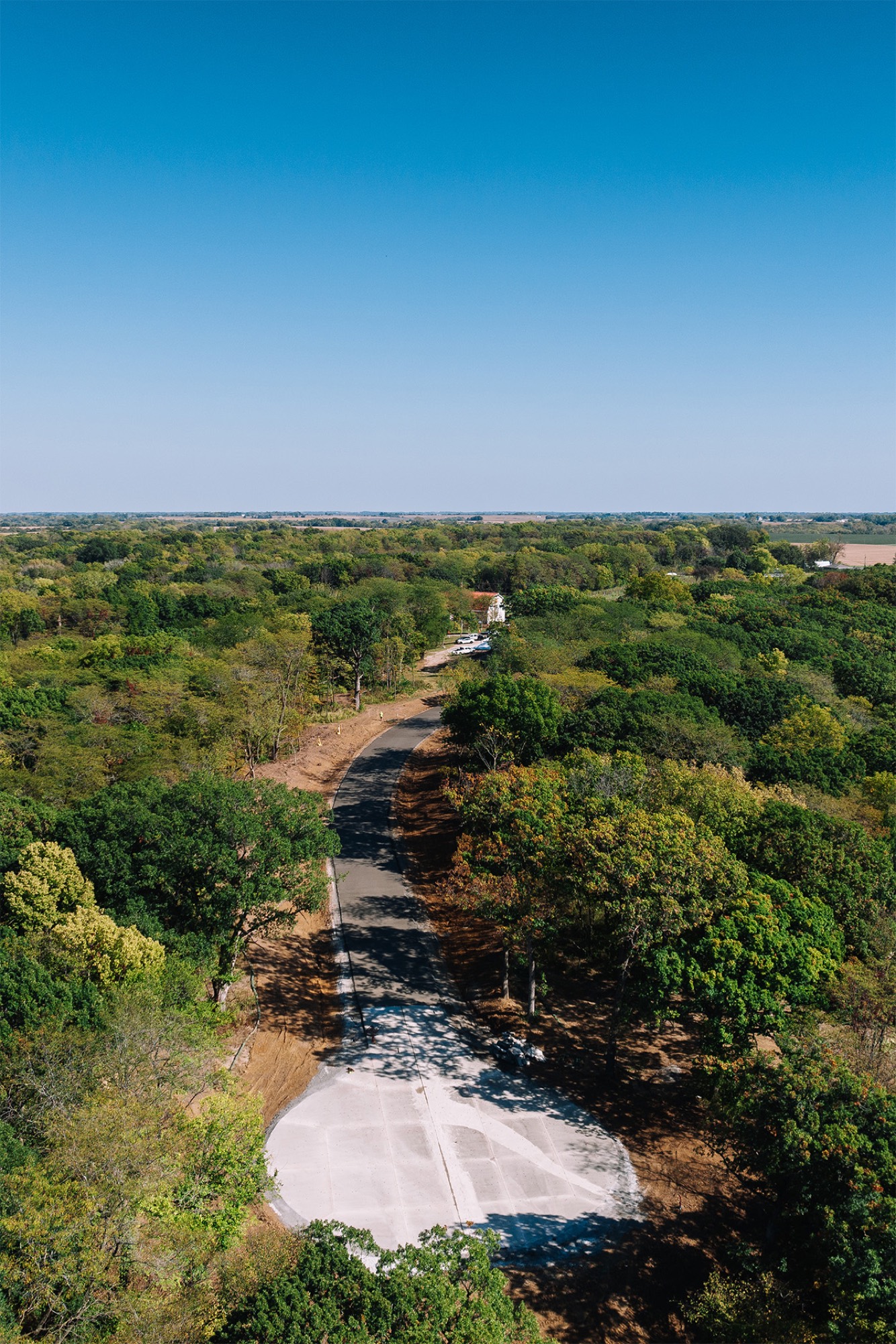 Aerial view of a freshly paved cul-de-sac curving through dense timber toward the horizon at Summerset Estates